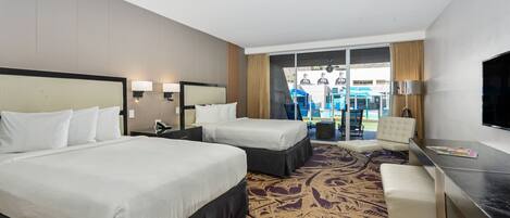 A hotel room with two beds, a desk, a chair, and a view of the outdoor area.