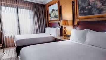 Habitación de hotel con dos camas, un escritorio, una silla, una lámpara y dos cuadros en la pared.