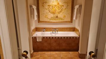 A bathroom with a large bathtub, a framed artwork above the sink, and a checkered tile border at the entrance.