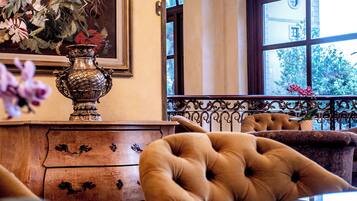 Una habitación con un aparador de madera, un jarrón grande y ornamentado, y dos sillones tapizados.