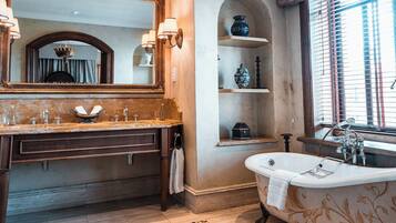 A classic bathroom with a freestanding bathtub, a double vanity with a mirror, and a shelf with decorative items.