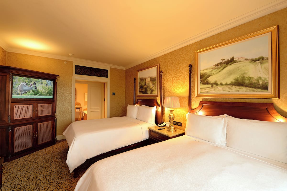 A hotel room with two beds, a television, a painting, and a wooden cabinet.