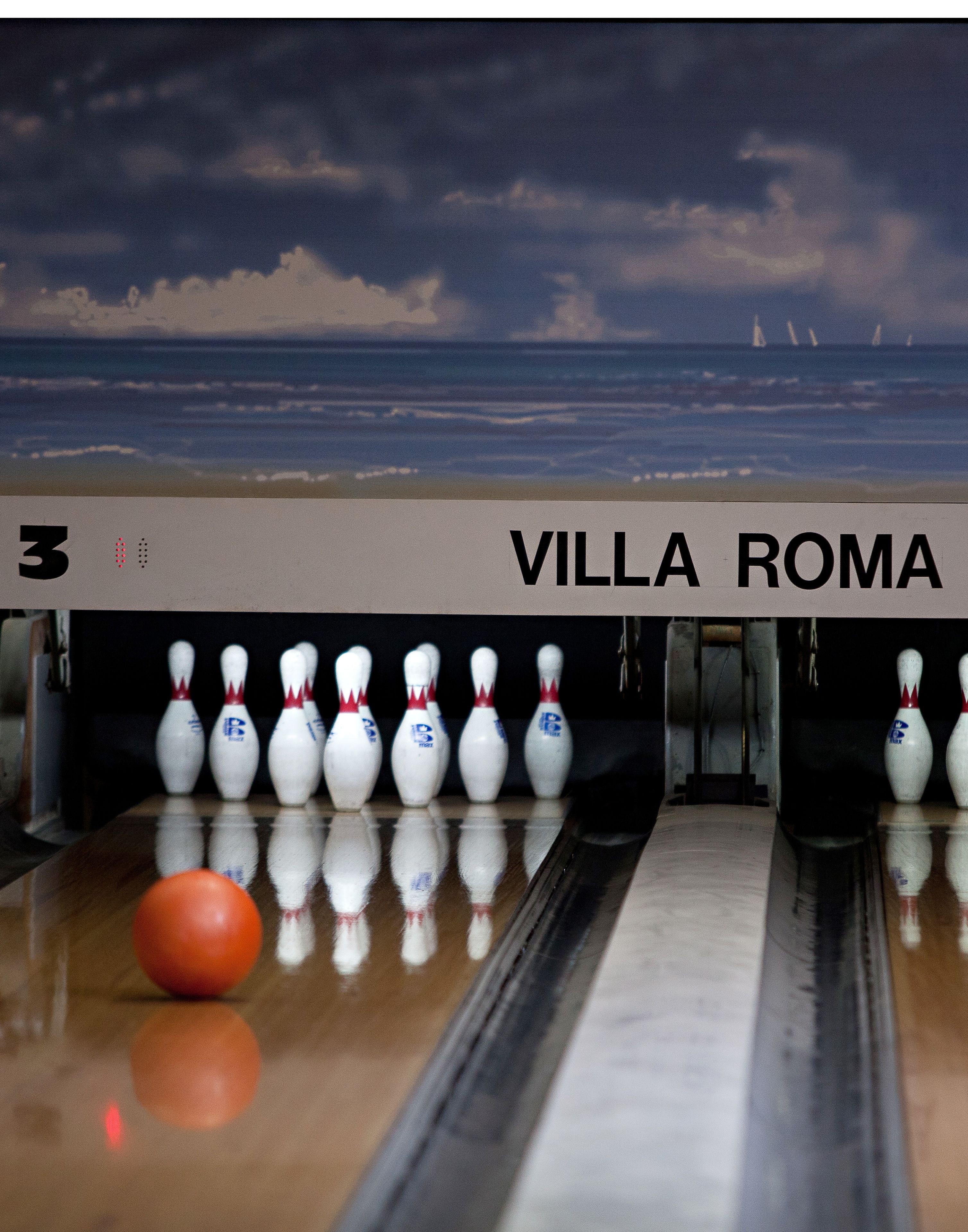 A bowling alley with a sign reading "VILLA ROMA" and a bowling ball in motion.