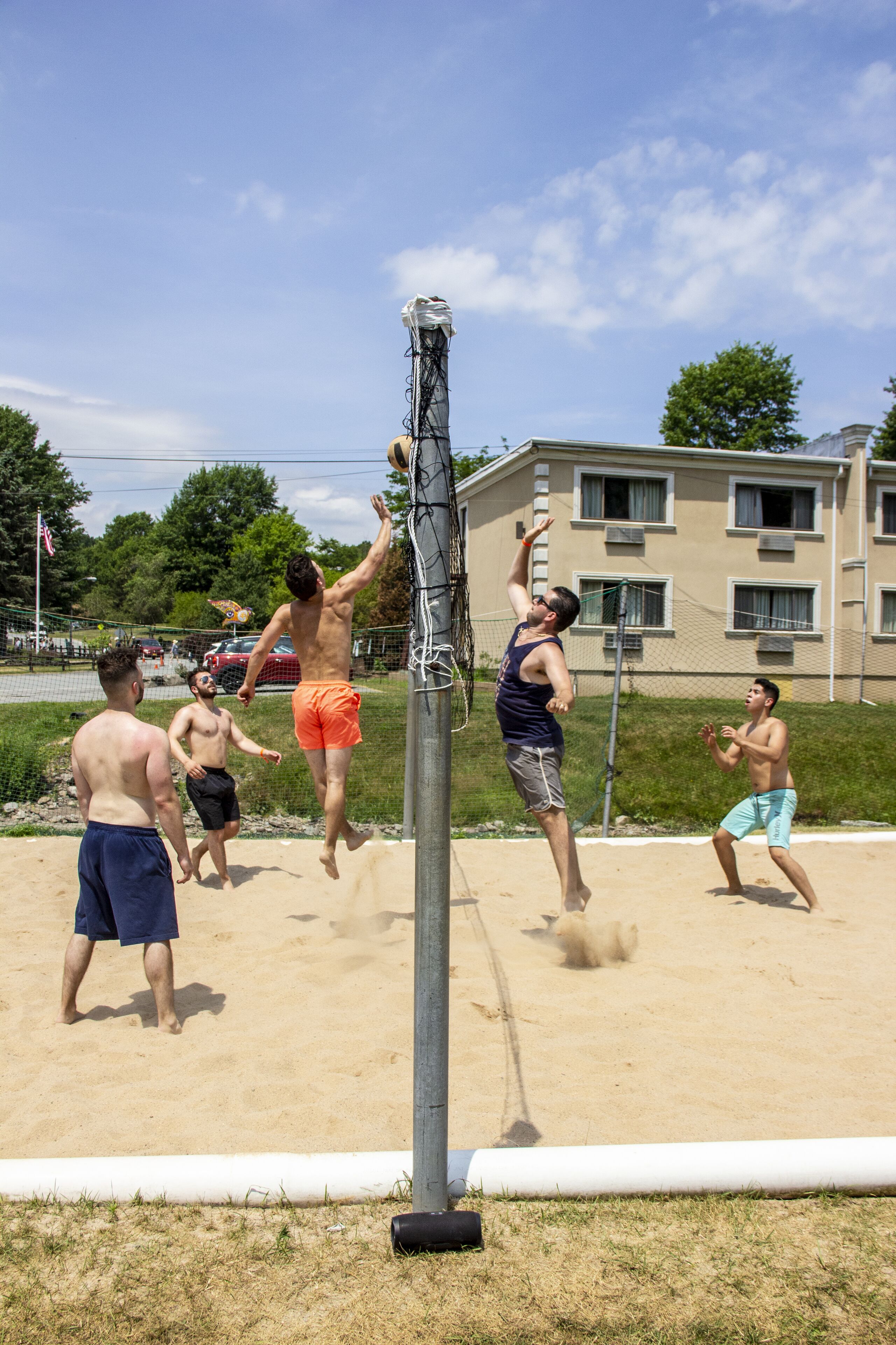Ein Volleyballspiel auf einem Sandplatz mit Netz, umgeben von Gebäuden und blauem Himmel.