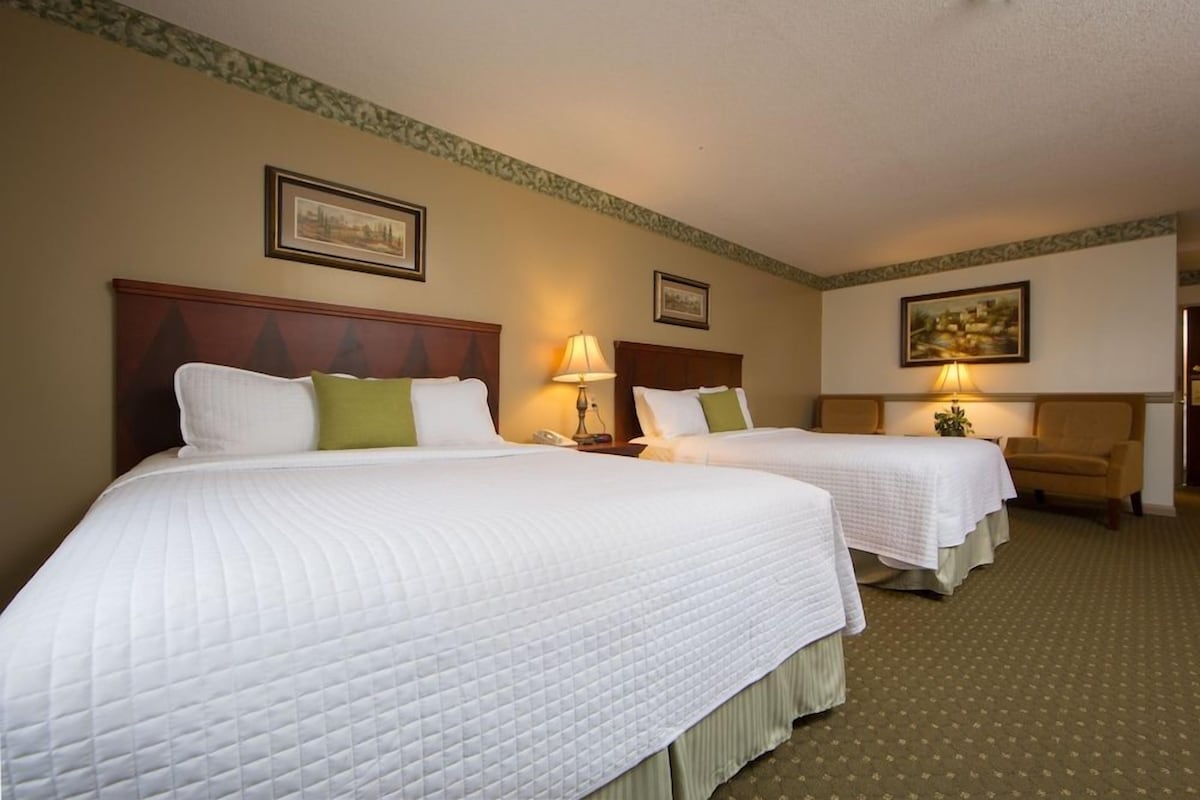 A hotel room with two beds, each with a white quilted bedspread and pillows, a wooden headboard, a lamp on each nightstand, and a framed picture on the wall.