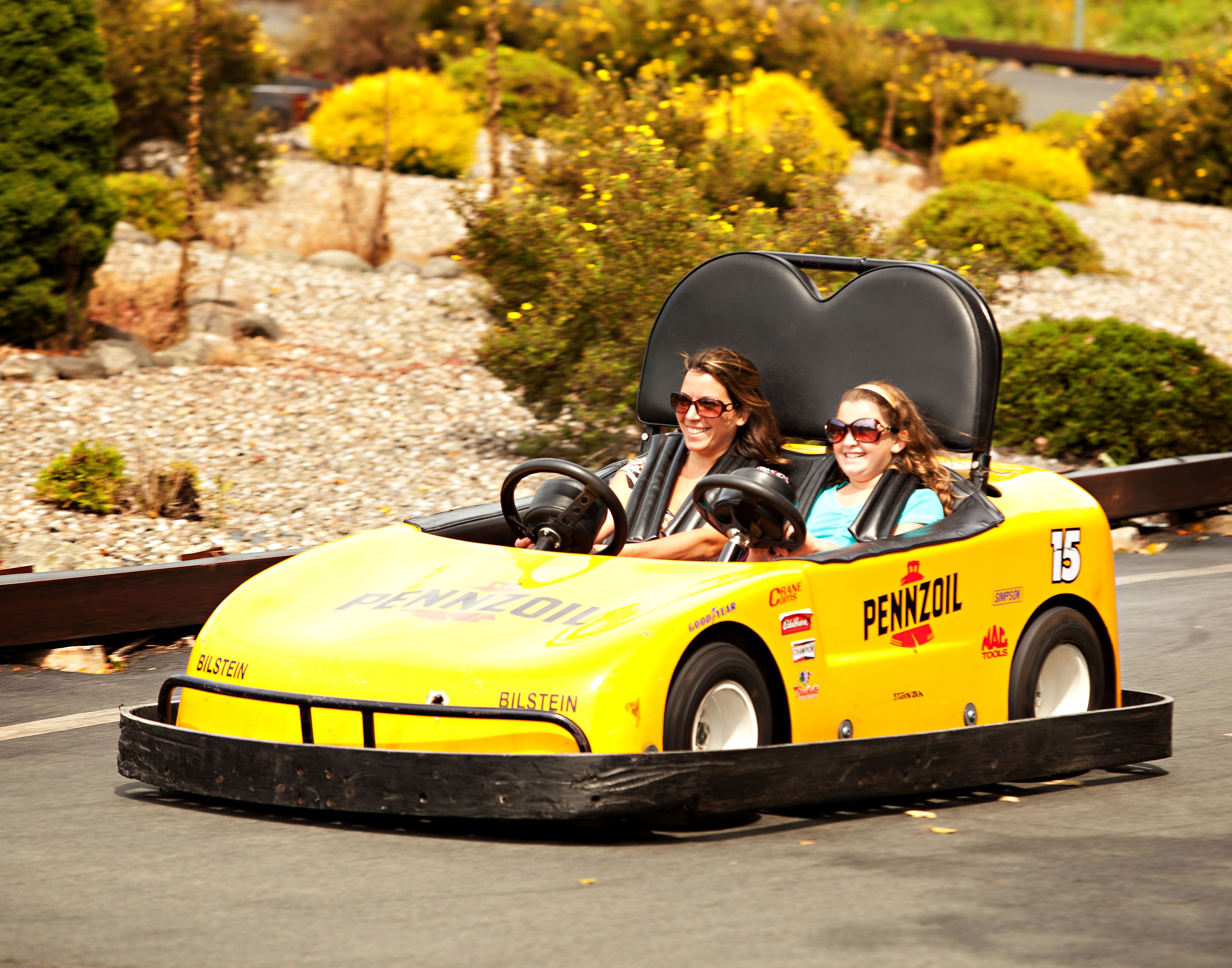 Een gele go-kart met 'PENNZOIL'-reclame, rijdend op een geasfalteerde weg.