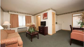 Een hotelkamer met een bank, een tafel met een lamp, een televisie, een dressoir en een deur naar een badkamer.