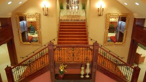 Uma escadaria imponente com grades ricamente decoradas e um lustre no topo.