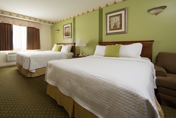 A hotel room with two beds, a chair, a lamp, and framed pictures on the wall.