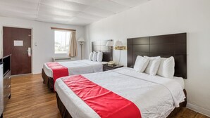 Ein Hotelzimmer mit zwei Betten, einem Schreibtisch, einem Stuhl, einer Lampe und einem fensterbepflanzten Fenster.