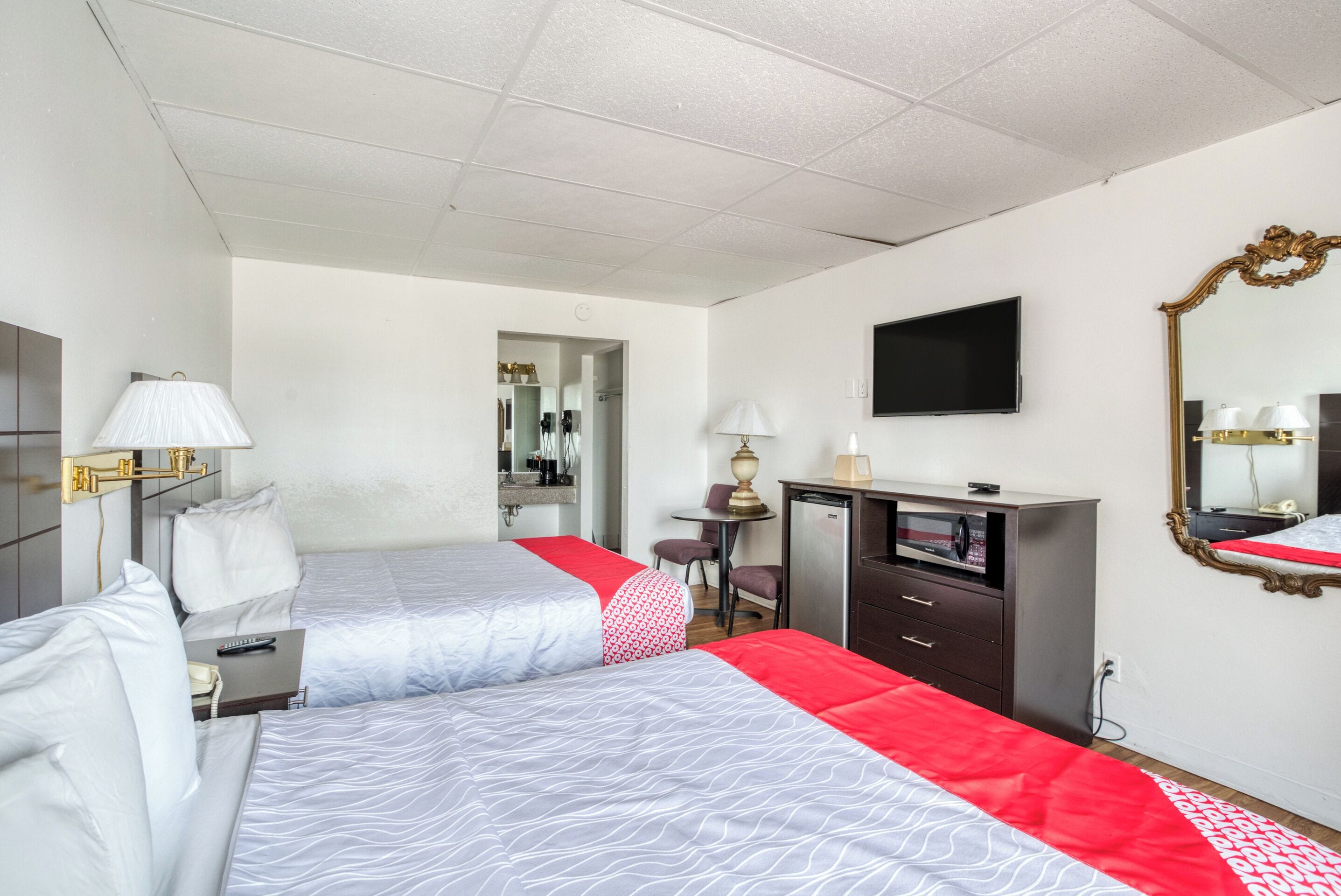 Une chambre d’hôtel avec deux lits, une télévision, un bureau avec une lampe, un miroir et une armoire.