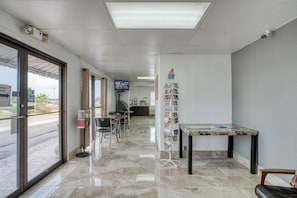 A hotel lobby with a reception desk, a television mounted on the wall, a bulletin board with various items, and a large window providing a view of the outside. - Lackland Gateway Inn (San Antonio)