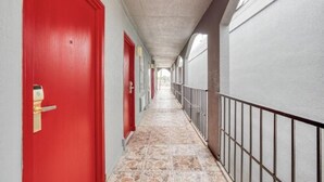 Un pasillo con puertas rojas, suelo de baldosas y barandilla de metal a un lado.