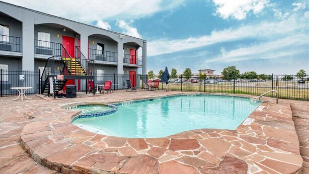 Un área de piscina con baldosas de piedra, una puerta roja y un balcón cercado.