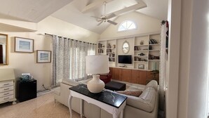 A living room with a ceiling fan, a sofa, a TV, and a bookshelf. - The Independent Inn - Formerly Heron House Court  (Key West)