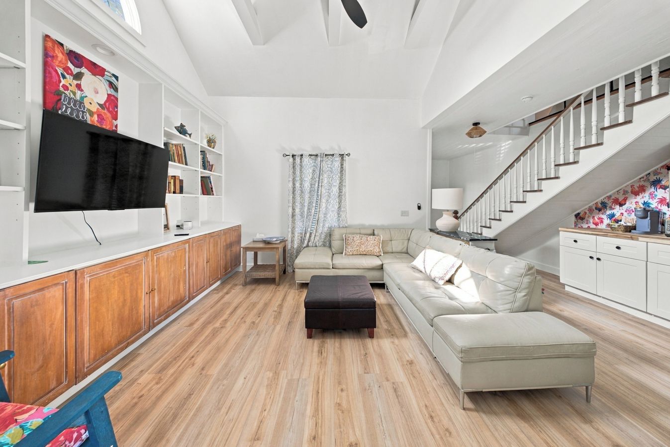 Amplia sala de estar con un televisor de pantalla plana grande, armarios de madera, un sofá color beige y una escalera.