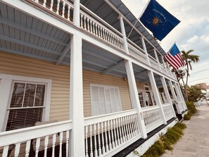A two-story building with a balcony, a flag, and a palm tree. - The Independent Inn - Formerly Heron House Court  (Key West)