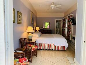 A bedroom with a bed, two bedside lamps, a chair, a small table, and a television. - The Independent Inn - Formerly Heron House Court  (Key West)