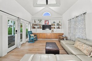 A spacious living room with a large window, a television, a bookshelf, and a seating area with a sofa and a rocking chair. - The Independent Inn (Key West)