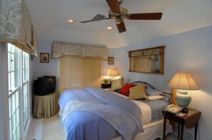 A bedroom with a bed, a ceiling fan, a bedside lamp, a nightstand, a telephone, and a window with blinds. - The Independent Inn - Formerly Heron House Court  (Key West)