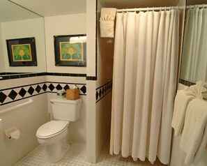 A bathroom with a toilet, a shower curtain, and two framed pictures on the wall. - The Independent Inn - Formerly Heron House Court  (Key West)