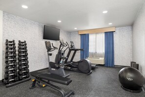 A gym with exercise equipment, a wall-mounted TV, and a window with curtains.