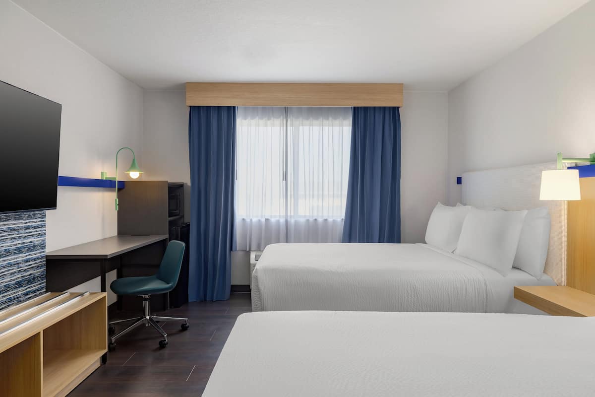 A hotel room with two beds, a desk, a chair, a TV, and a window with curtains.