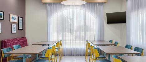 A conference room with a long table, yellow chairs, a red couch, and a TV mounted on the wall.