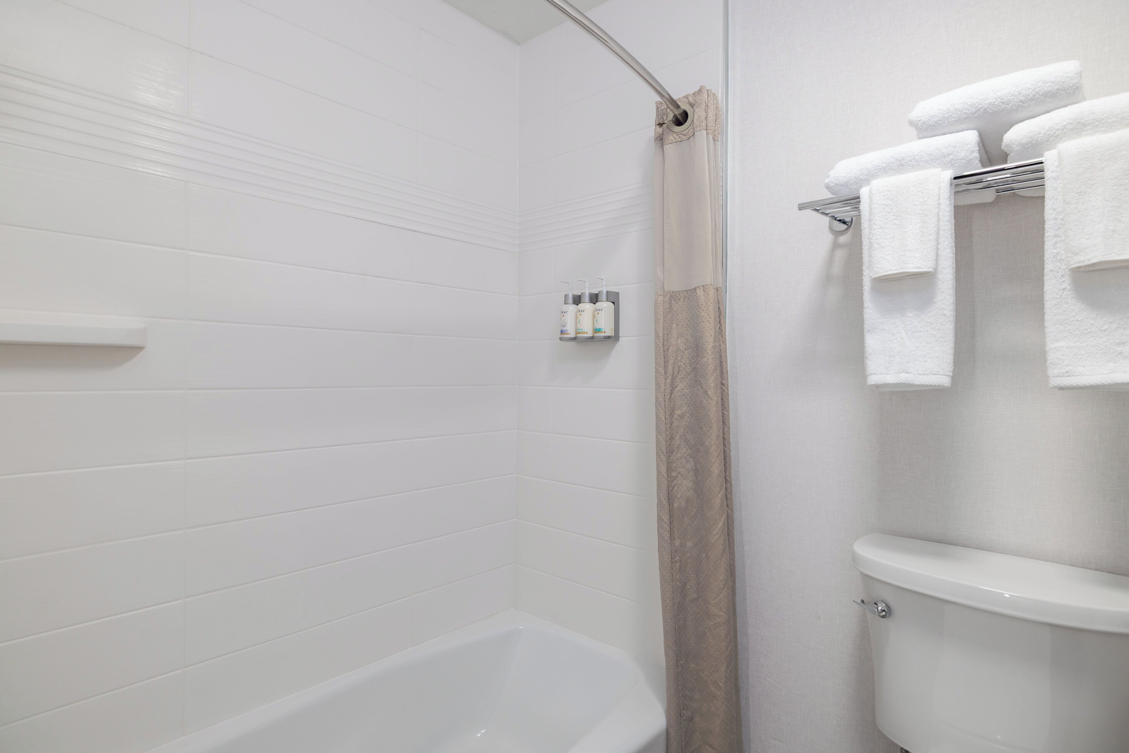 Une salle de bain avec des murs carrelés de carreaux blancs, une baignoire, un rideau de douche et des toilettes.