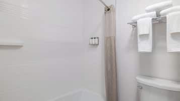 Une salle de bain avec des murs carrelés de carreaux blancs, une baignoire, un rideau de douche et des toilettes.