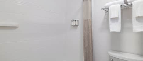 A bathroom with white tiled walls, a bathtub, a shower curtain, and a toilet.