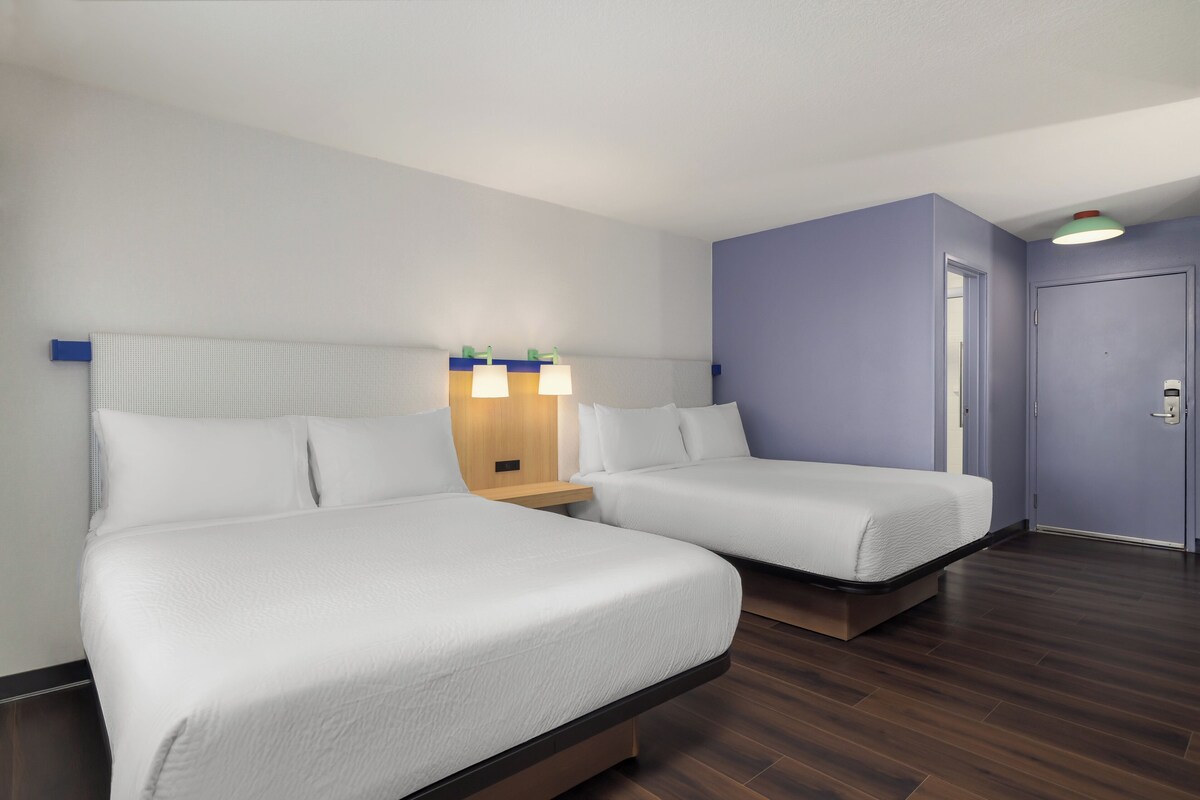 Ein Hotelzimmer mit zwei Betten, einem Nachttisch mit Lampe und einer Tür.