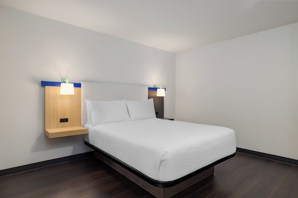 Quarto de hotel moderno com uma cama de solteiro, duas mesas de cabeceira com abajures e uma cabeceira embutida.