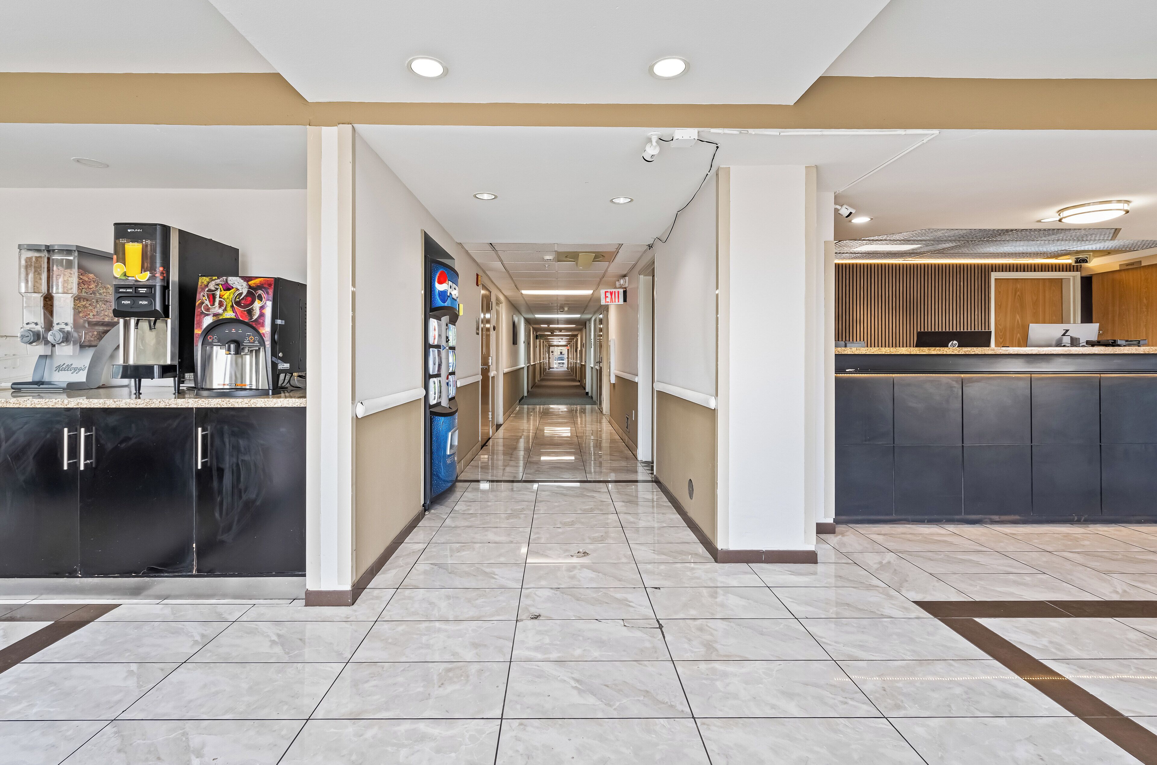 A hotel corridor with a coffee station, a Pepsi refrigerator, and a reception desk.