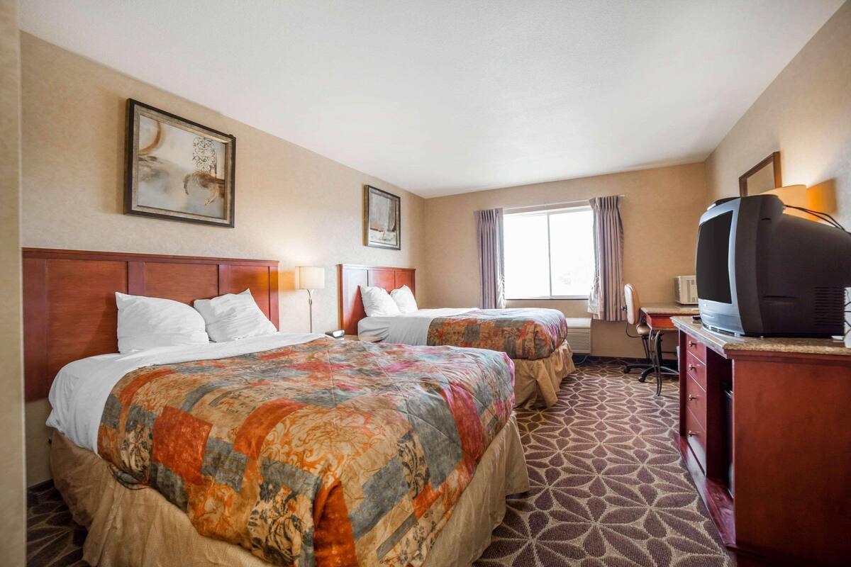 A hotel room with two beds, a television, a desk, and a window with curtains.