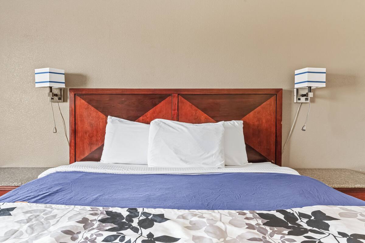 A neatly made bed with a wooden headboard, white pillows, and a blue bedspread.