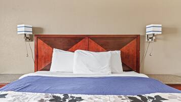 Una cama bien tendida con cabecera de madera, almohadas blancas y colcha azul.