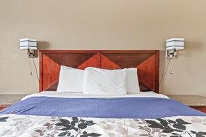 Una cama bien tendida con cabecera de madera, almohadas blancas y colcha azul.