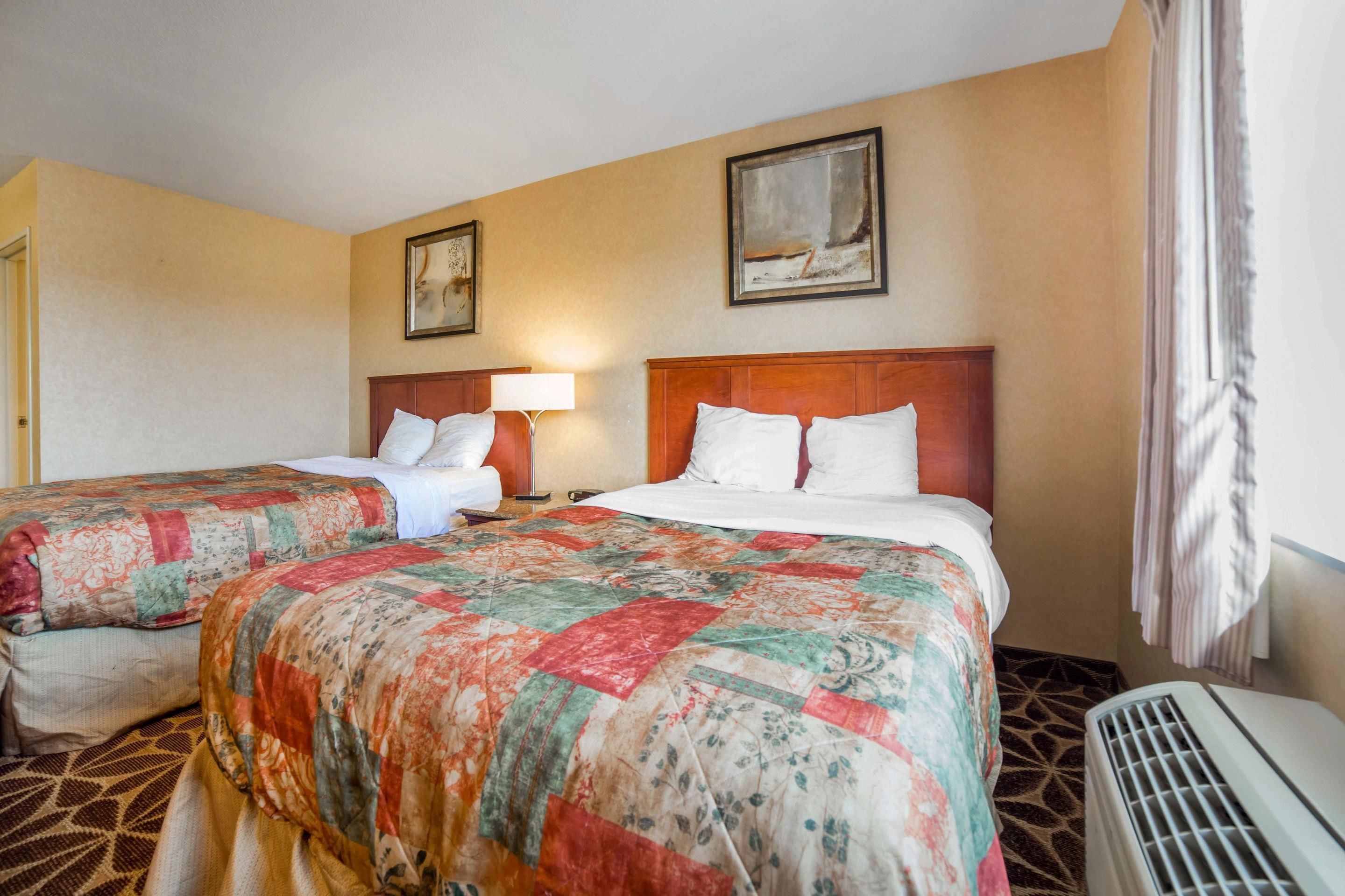 A hotel room with two beds, a large window with curtains, and a radiator.