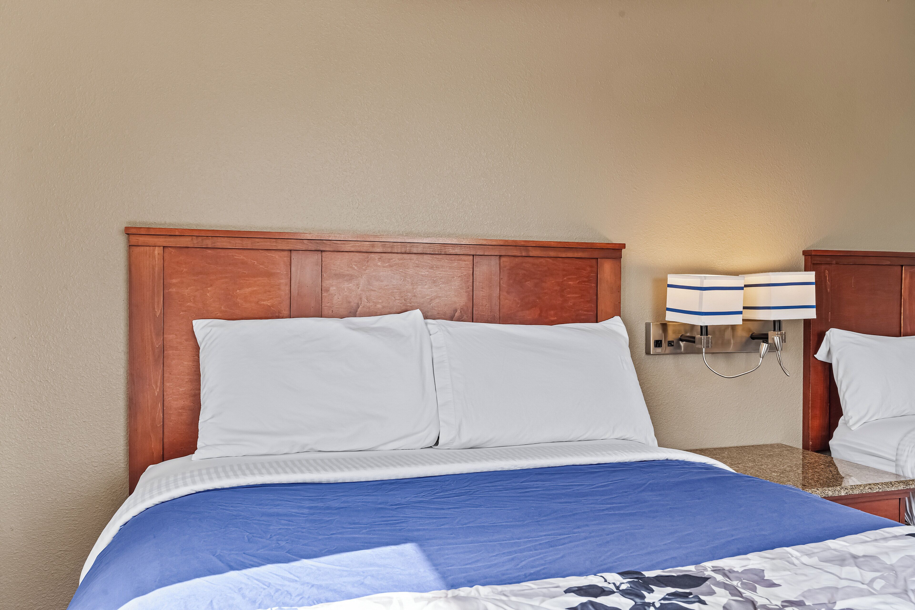 A hotel room with a wooden headboard, a bed with white and blue bedding, and a wall-mounted lamp.