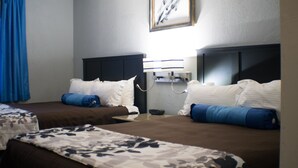 A hotel room with two beds, a bedside table, a wall-mounted lamp, and a framed picture.