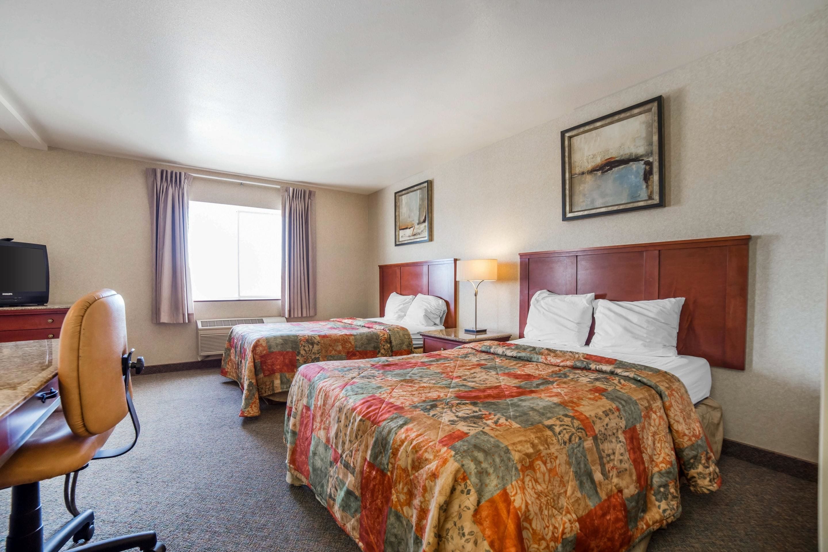 A hotel room with two beds, a desk, a chair, a television, and a painting on the wall.