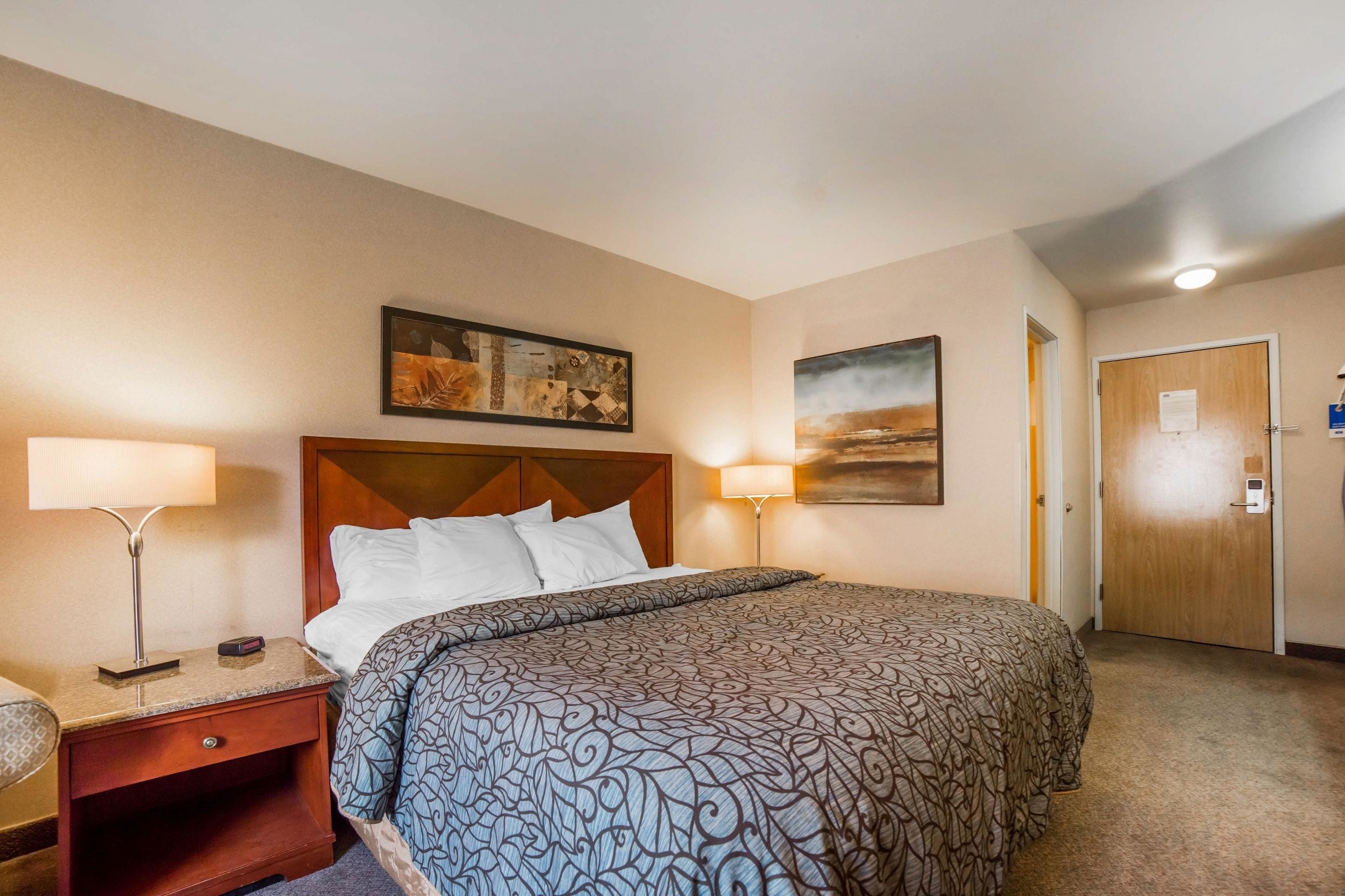 A hotel room with a large bed, two bedside lamps, a nightstand, and a door with a lock.