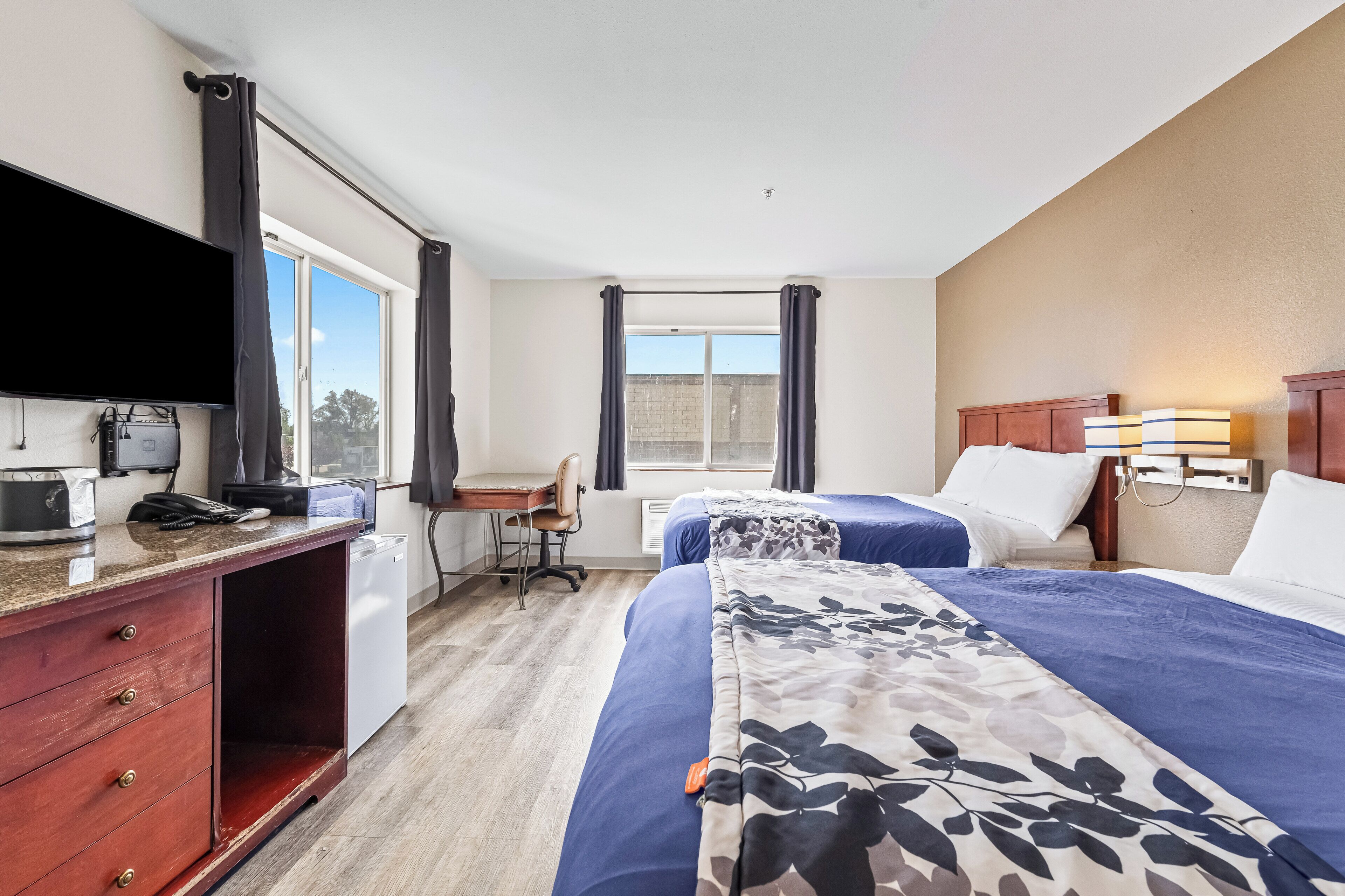 Una habitación de hotel con dos camas, un escritorio, una silla, un televisor y un ventanal con cortinas.