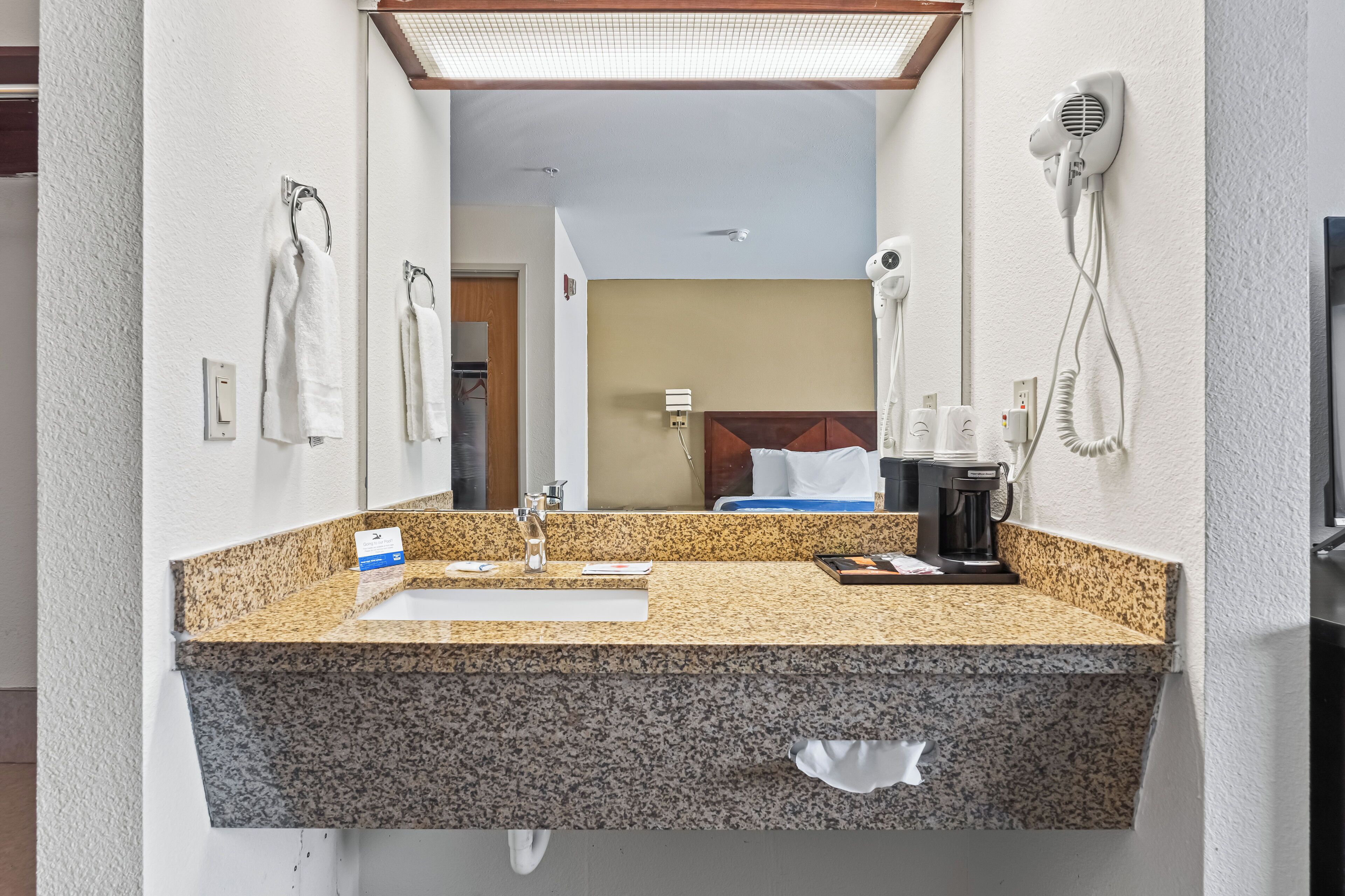 A bathroom with a granite countertop sink, a mirror, a hairdryer, and a towel rack.