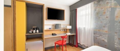Una habitación de hotel con una cama, un escritorio con silla, un televisor y un armario.