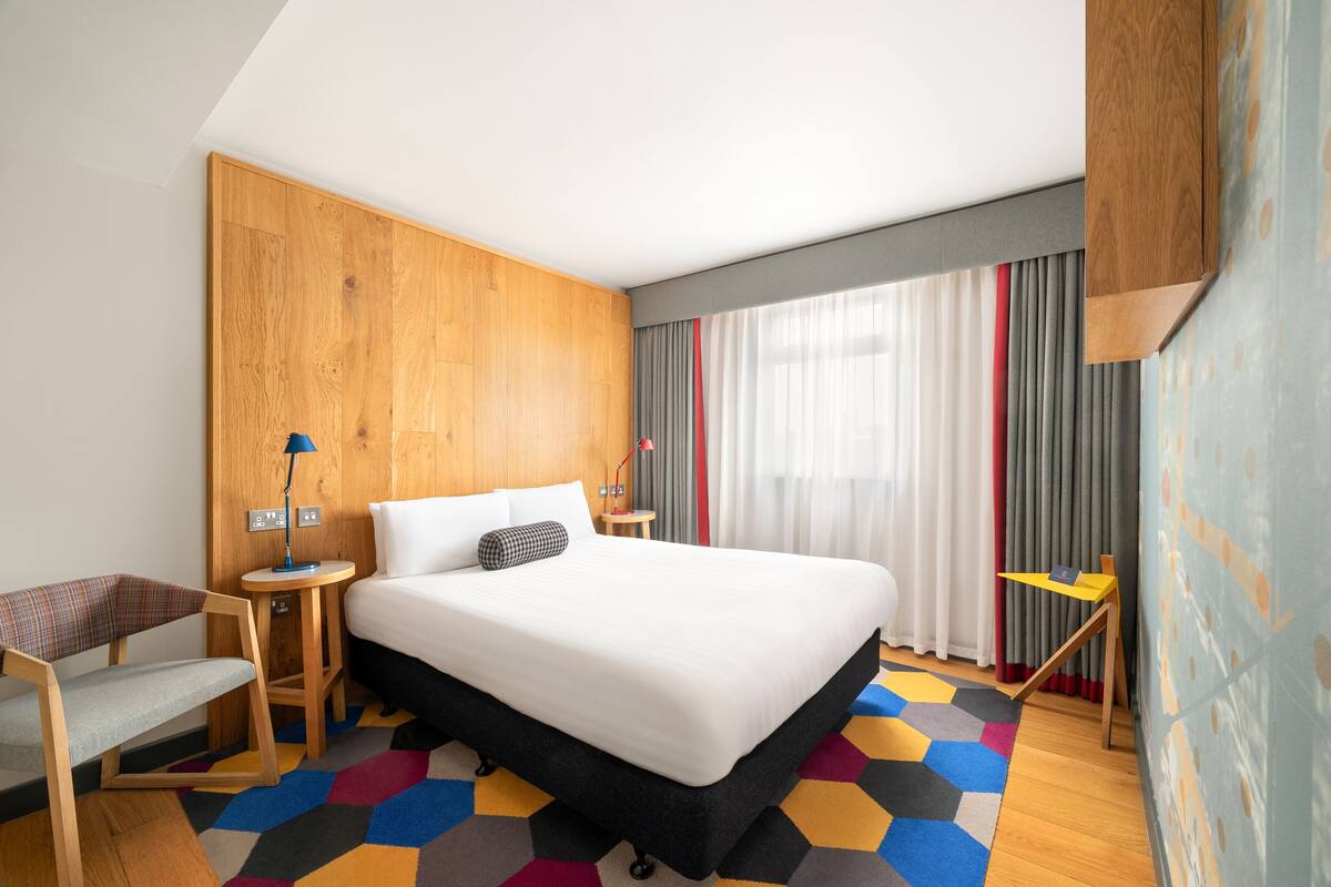 Habitación de hotel con una cama grande, un escritorio, una silla y un tapete colorido.