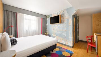A modern hotel room with a large bed, a TV mounted on the wall, a desk, and a red chair.
