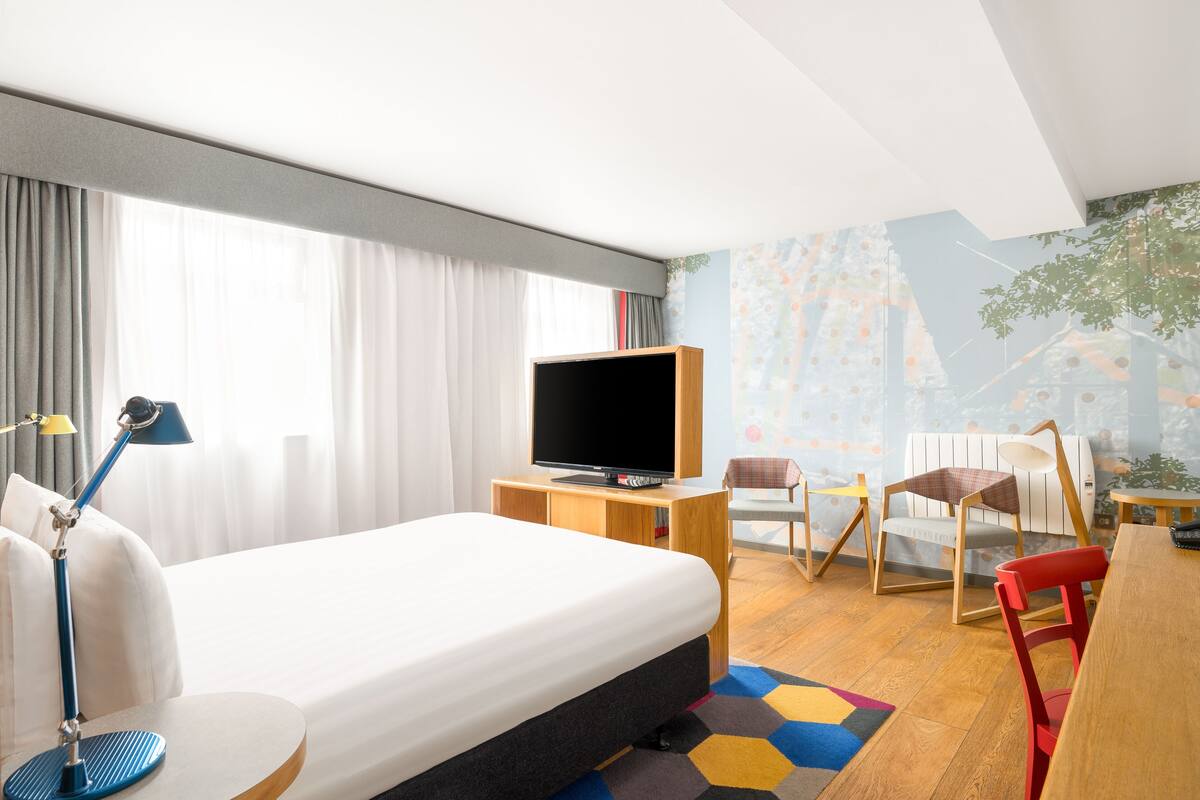 Una habitación de hotel con una cama, un televisor sobre un mueble de madera, un escritorio y una silla.