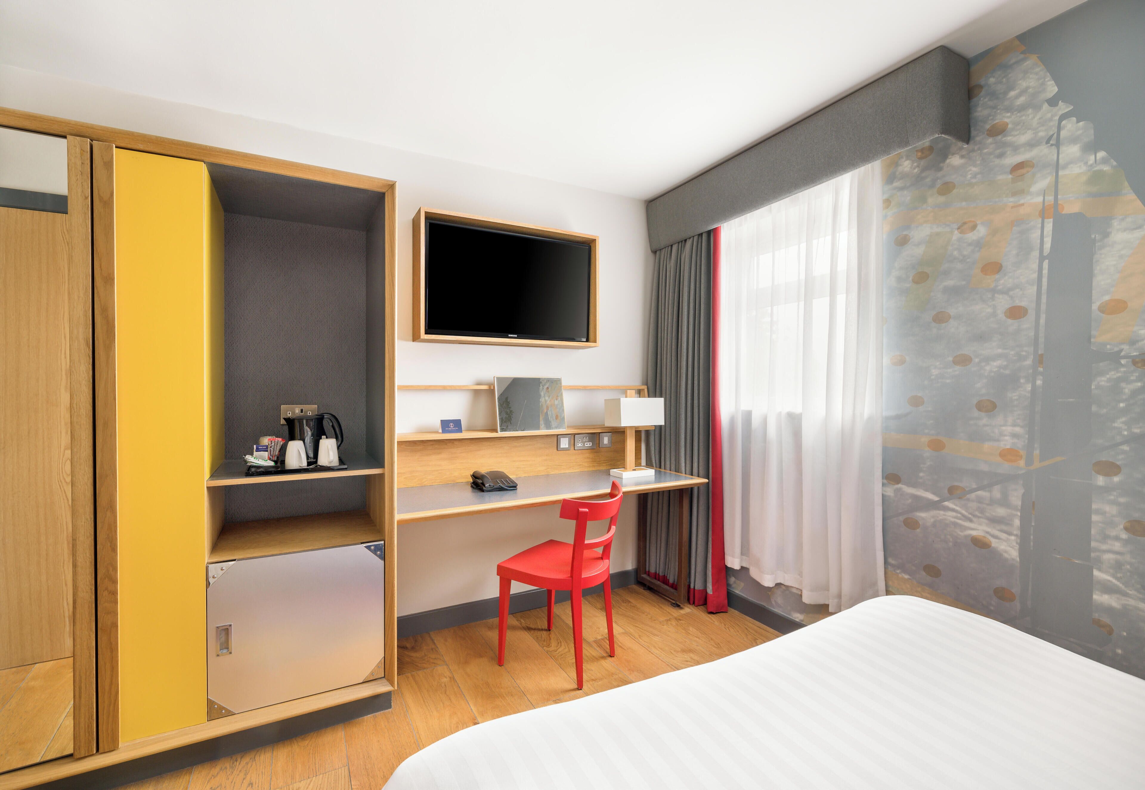 Una habitación de hotel con cama, escritorio con silla, televisión y armario.